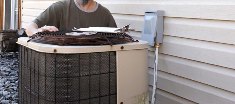 Technician inspecting an old outdoor air conditioning unit next to a house