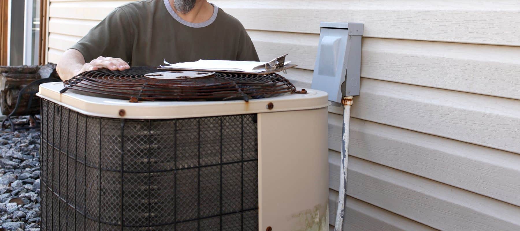 Technician inspecting an old outdoor air conditioning unit next to a house