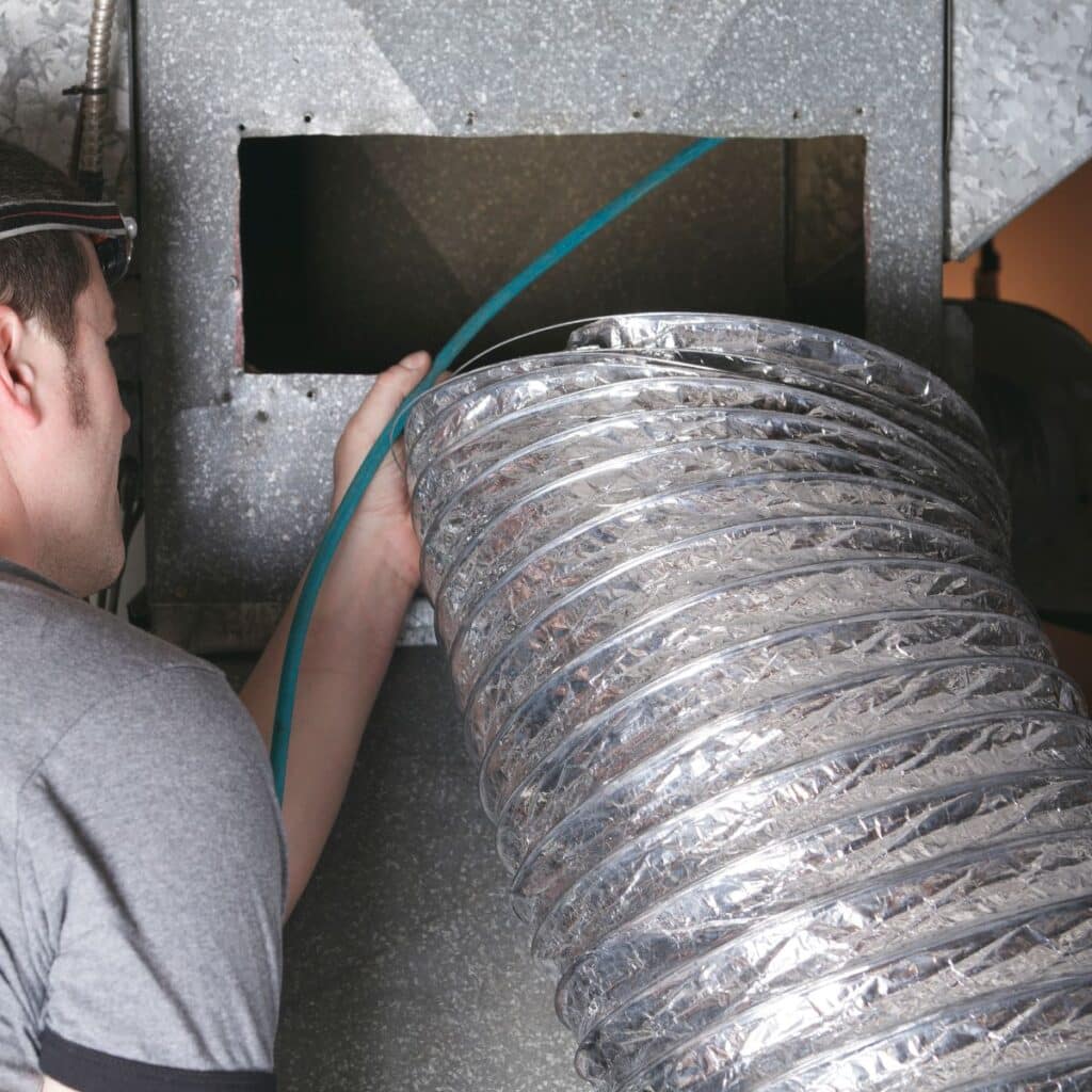 Technician cleaning or inspecting an air duct using a flexible vacuum hose