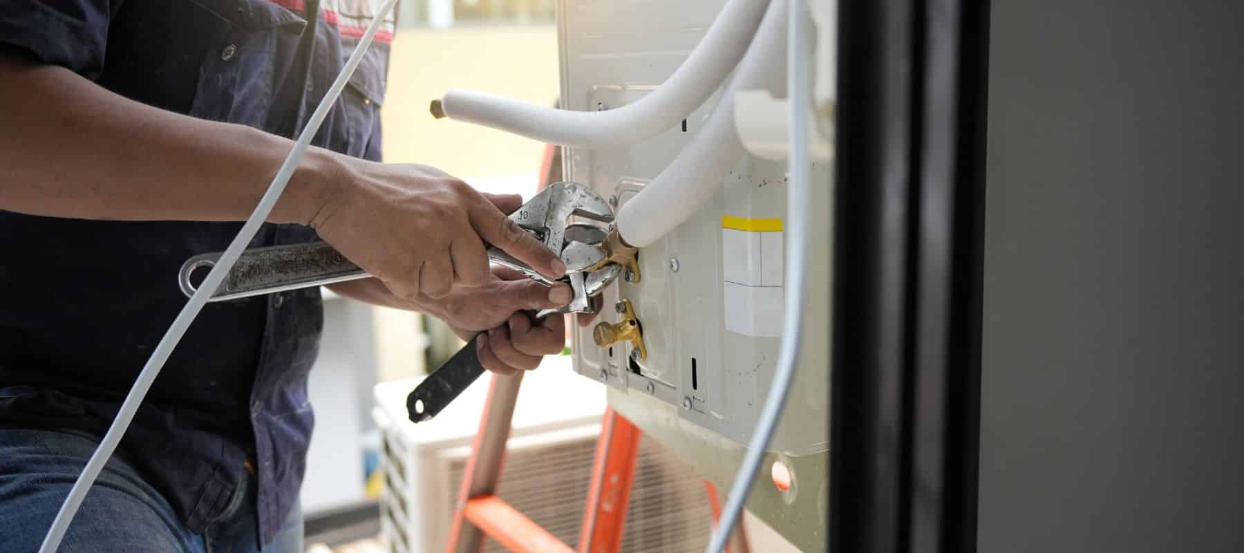 Technician tightening connections on an air conditioning unit using wrenches