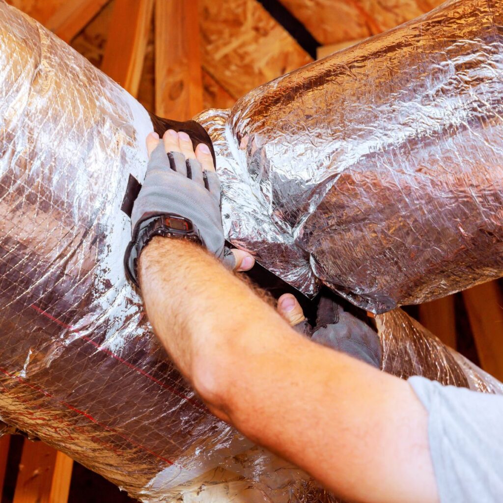 Technician sealing insulated HVAC ductwork in an attic space